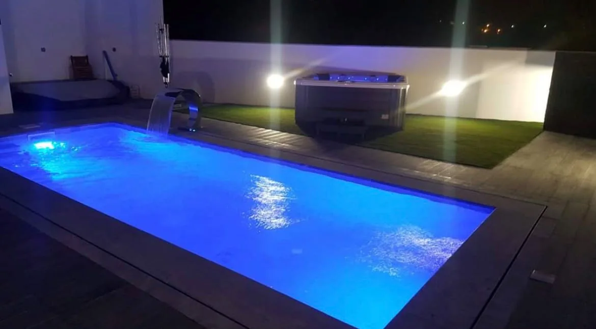 Piscina iluminada ao anoitecer, com espaço de lazer exterior